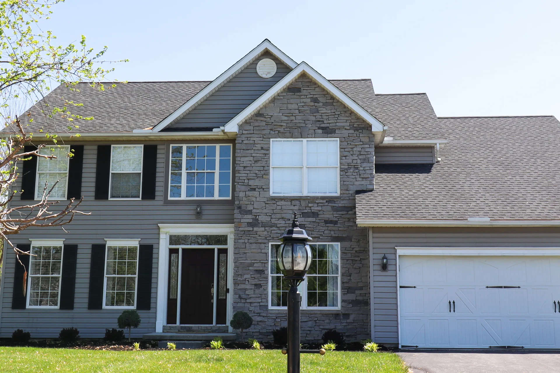 Completed roof on a stone-front home with grey siding in York County, PA by Cool Water Roofing